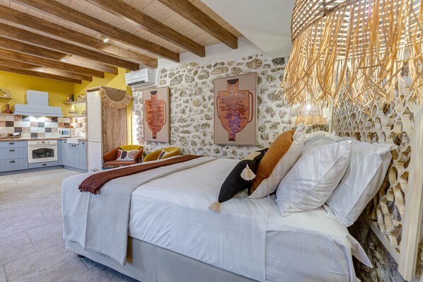 A bedroom with a bed, pillows, a bedside table, a wall-mounted lamp, and a stone wall.