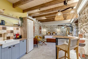 A rustic kitchen with a stone wall, wooden ceiling beams, and a dining area with a table and chairs.