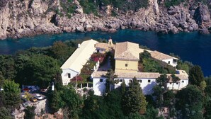 Une propriété située sur la côte, comprenant plusieurs bâtiments, une imposante structure blanche et un rivage rocheux.