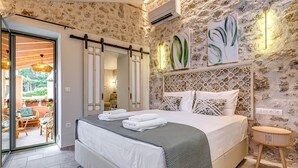 A bedroom with a bed, a wooden side table, a wall-mounted light, and a door leading to a balcony.