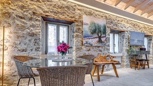 A stone-walled room with wicker furniture, a glass table, a painting of a tree, and a TV.