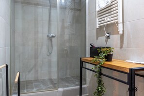 Une salle de bain moderne avec une douche à parois de verre, un meuble-lavabo en bois avec un évier noir et une plante en pot.