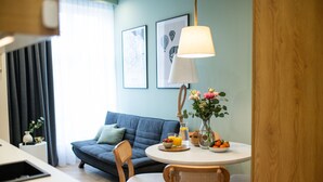 Ein modernes Wohnzimmer mit einem grauen Sofa, einem runden Esstisch mit Stühlen, einer Vase mit Blumen und einer Lampe.