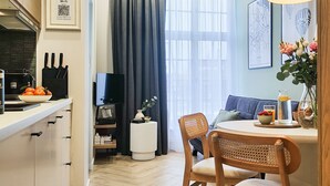 Eine moderne Küche mit Holzschränken, einem Essbereich mit rundem Tisch und Stühlen, einem Fernseher und einem Fenster mit Vorhängen.