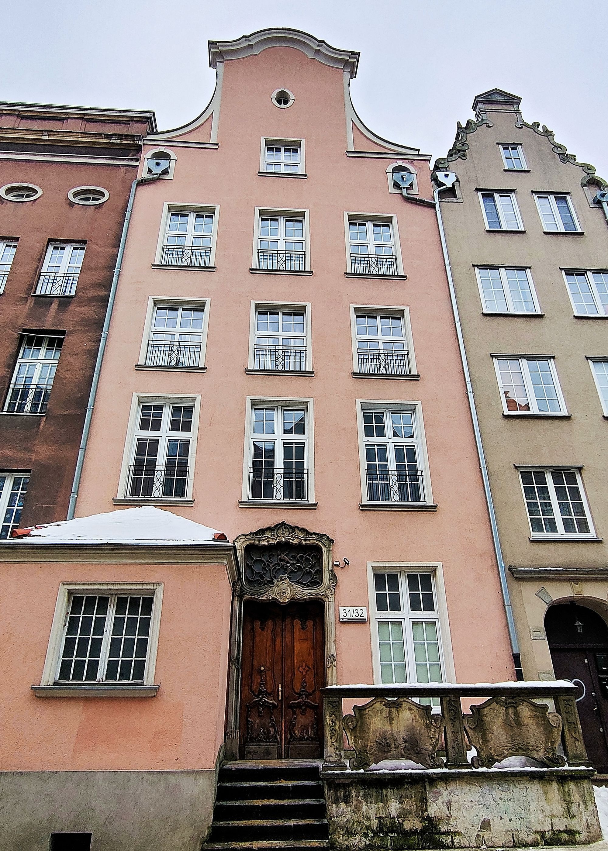 A multi-story building with a central entrance, multiple windows with balconies, and a staircase leading to the entrance.