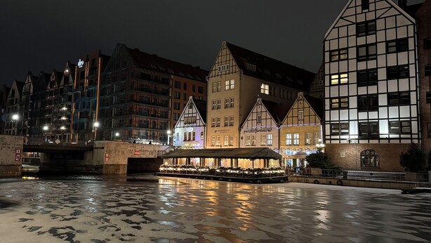 Blick auf eine historische Stadt mit traditioneller Architektur, einen Bootsanleger und eine Brücke, alles am Fluss gelegen.