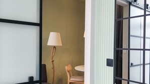 Ein Hotelzimmer mit Schiebetür, einem runden Tisch, einem Stuhl, einer Lampe und einem Bett mit grauer Decke.