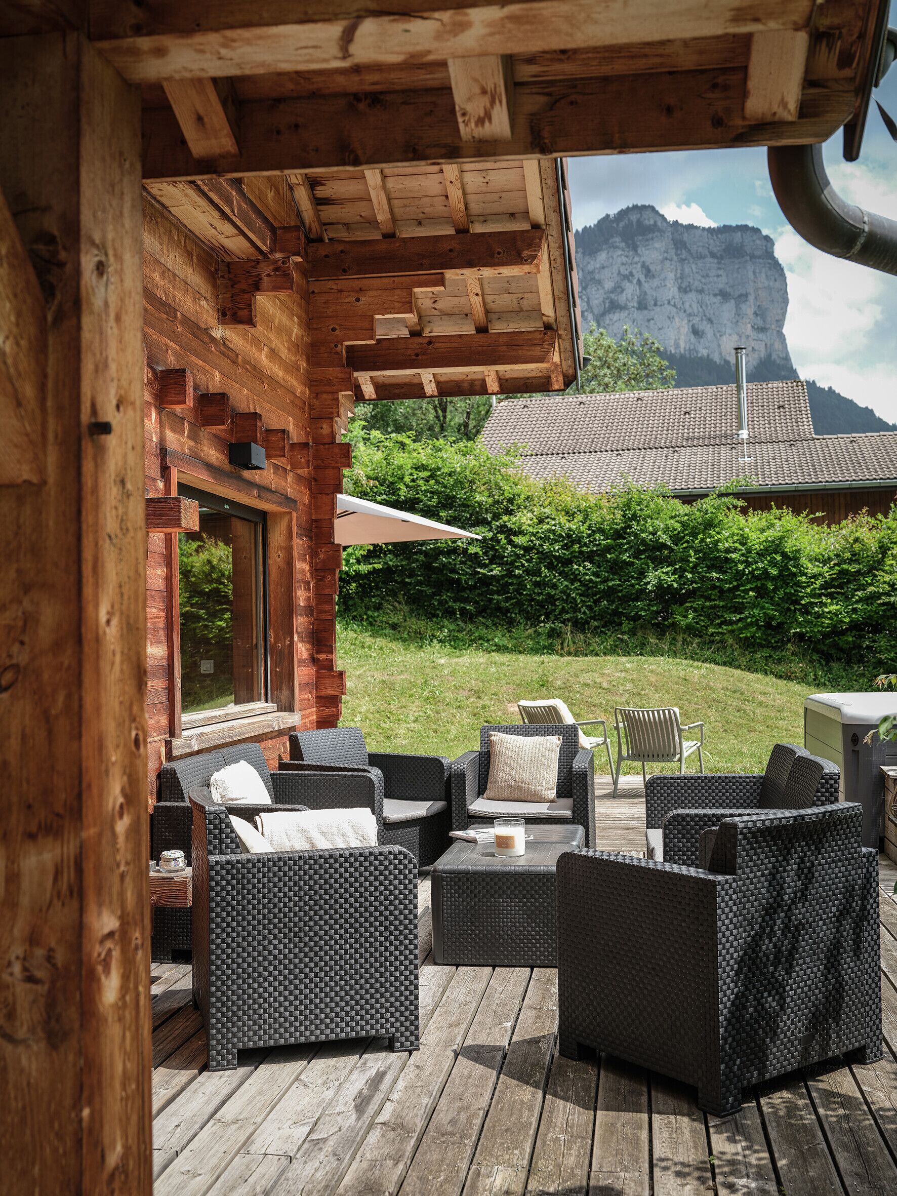 Eine Holzterrasse im Freien mit Korbmöbeln und Blick auf einen Berg.