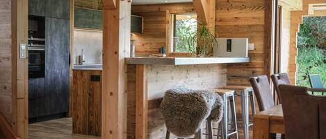 Eine moderne Küche mit Holzbalken, einem Essbereich mit Barhocker und Blick ins Freie.