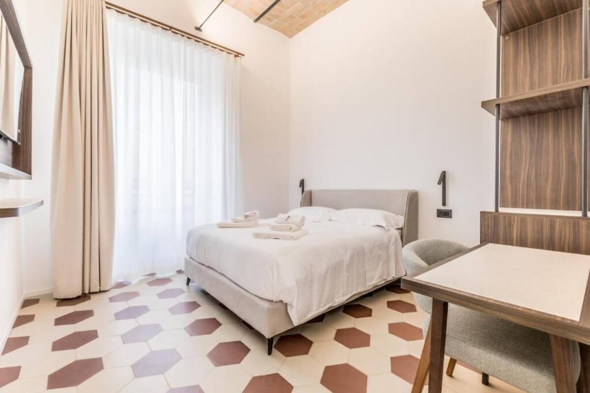 Ein modernes Hotelzimmer mit einem Bett, einem Schreibtisch und einem großen Fenster mit Vorhängen.