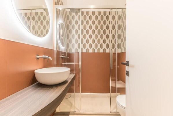 A modern bathroom with a round mirror, a white sink, and a shower enclosure.