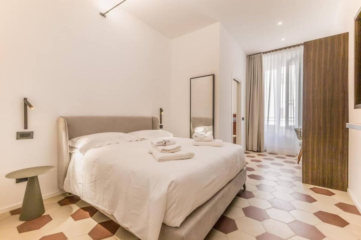 Ein modernes Hotelzimmer mit einem großen Bett, einem Nachttisch, einem Spiegel und einem geometrisch gemusterten Boden.