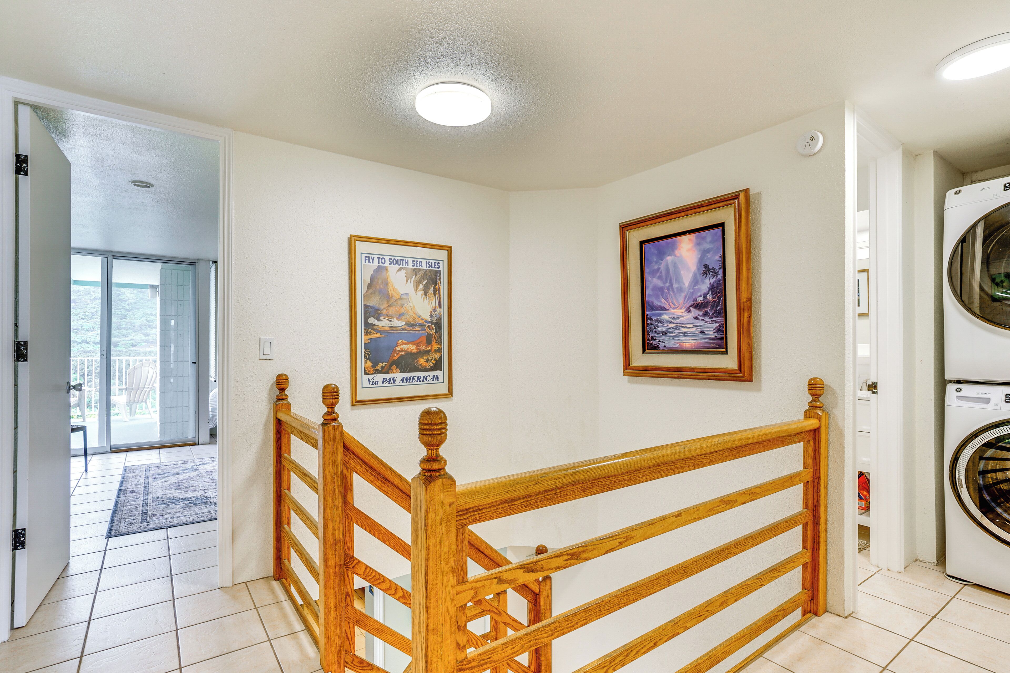 A hallway with a wooden staircase, a washing machine, and two framed pictures on the wall.