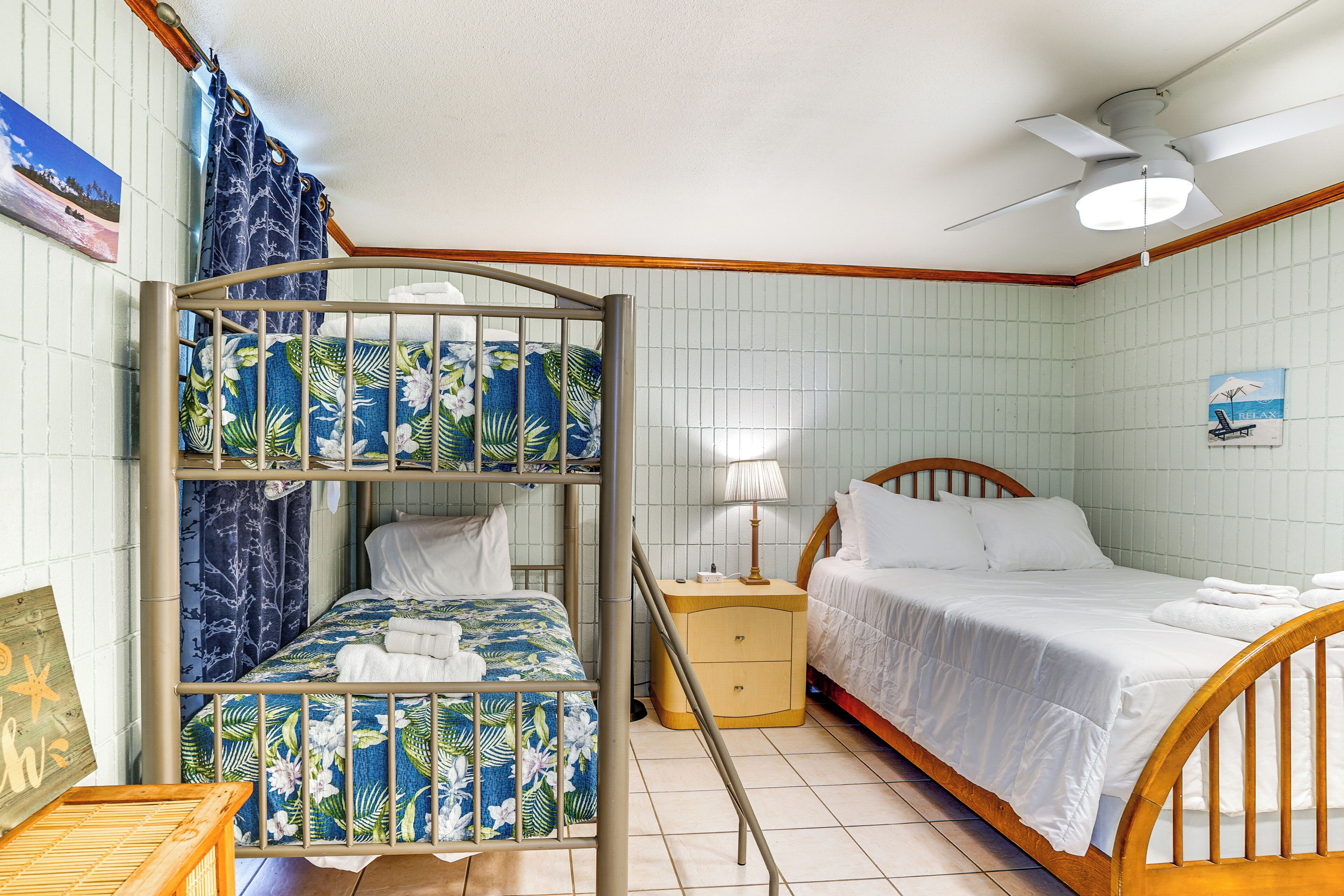 A room with bunk beds, a single bed, a nightstand, a lamp, and a ceiling fan.