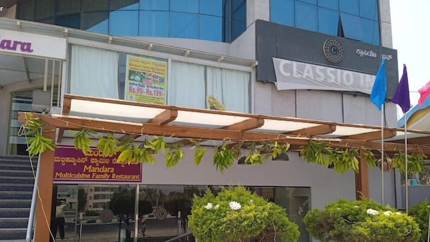 A building with a sign for 'Mandra Multicuisine Family Restaurant' and a 'CLASSIO' sign. There are two small trees in front of the entrance. - Classio Inn Hotel (Bengaluru)