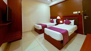 A hotel room with two beds, a TV, a ceiling fan, and a door. - Classio Inn Hotel (Bengaluru)