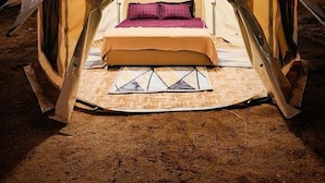 Een tent met een bed erin, omringd door zand.