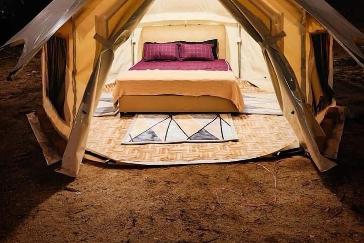 A tent with a bed inside, surrounded by a sandy ground.