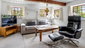 A living room with a sofa, a black leather chair, a wooden coffee table, a TV on a wooden stand, and a ceiling fan.