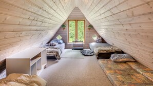An attic bedroom with a sloped ceiling, two beds, a desk, and a large window.