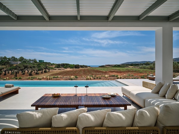 A poolside area with a view of a natural landscape, outdoor furniture, and a pergola structure.