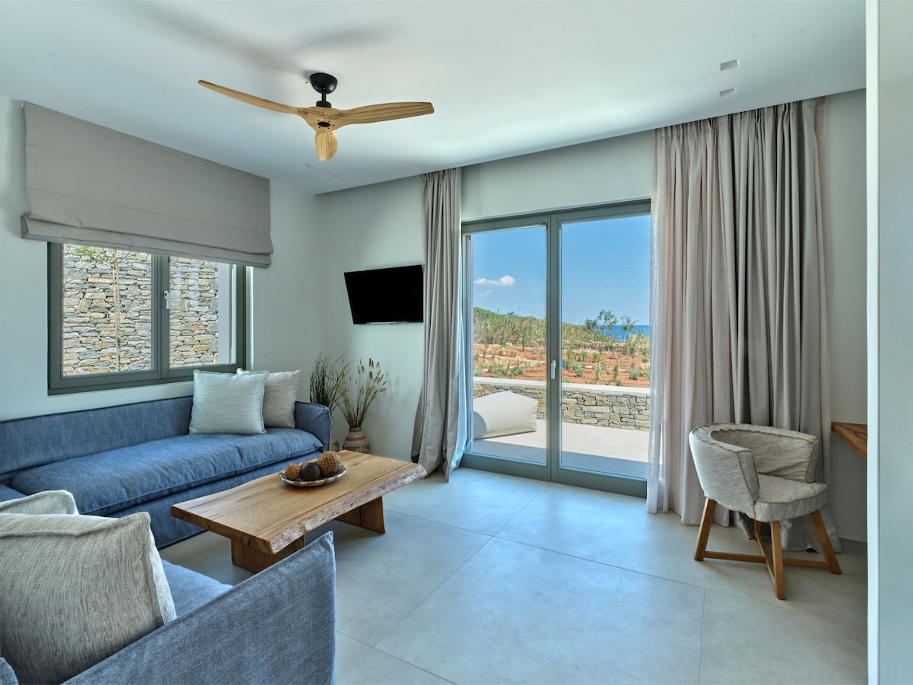 A modern living room with a blue sofa, a wooden coffee table, and a stone wall.