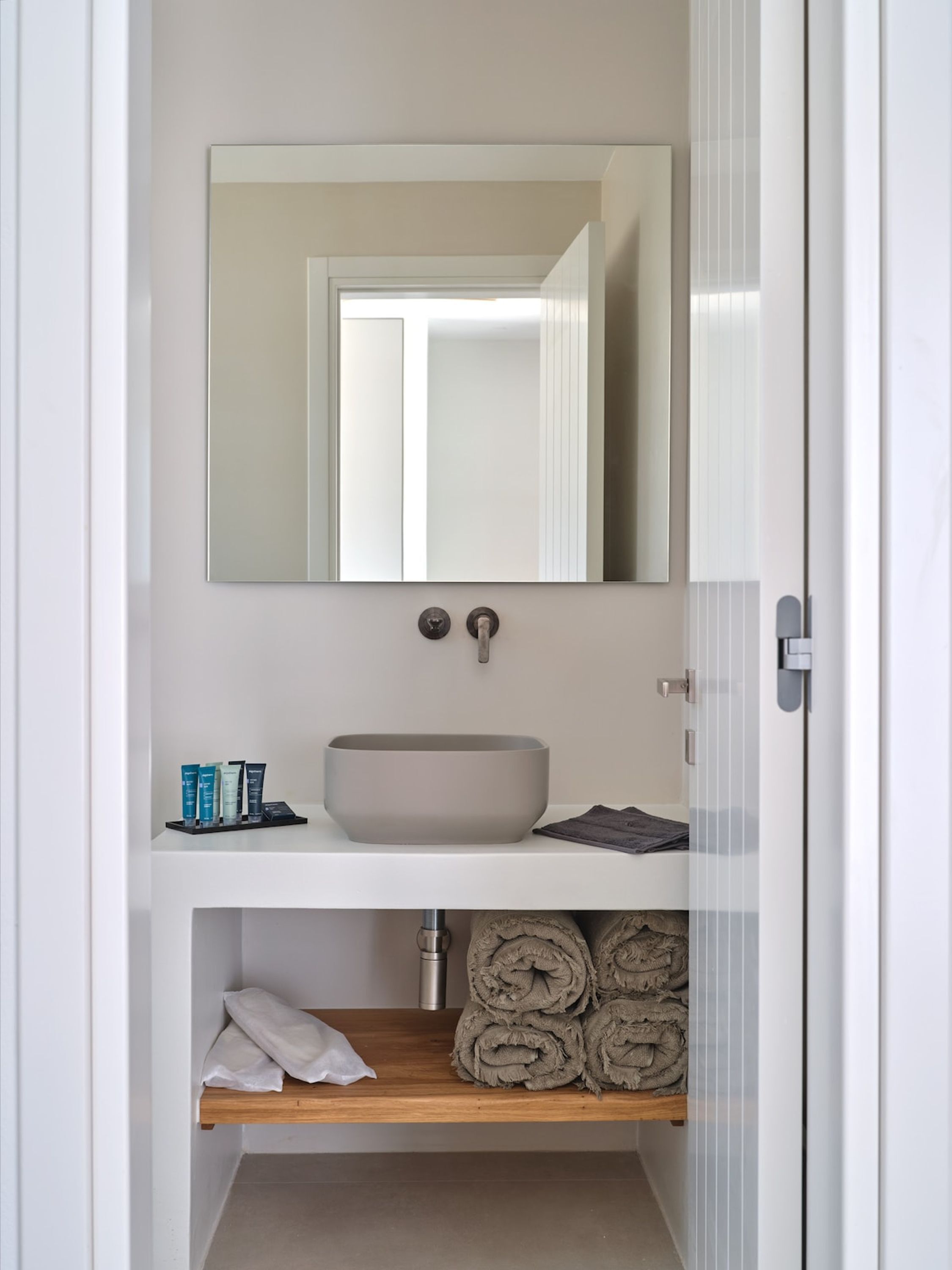 A bathroom with a white sink, a mirror above it, and a shelf below holding towels and toiletries.