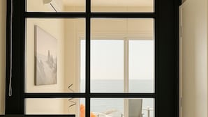 A hotel room with a large window offering a view of the sea, a bed, a desk, and a chair. - SeaRock Suites (Aamchit)