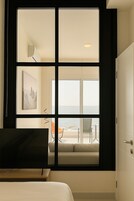 Habitación de hotel con un ventanal amplio que ofrece vistas al mar, una cama, un escritorio y una silla.