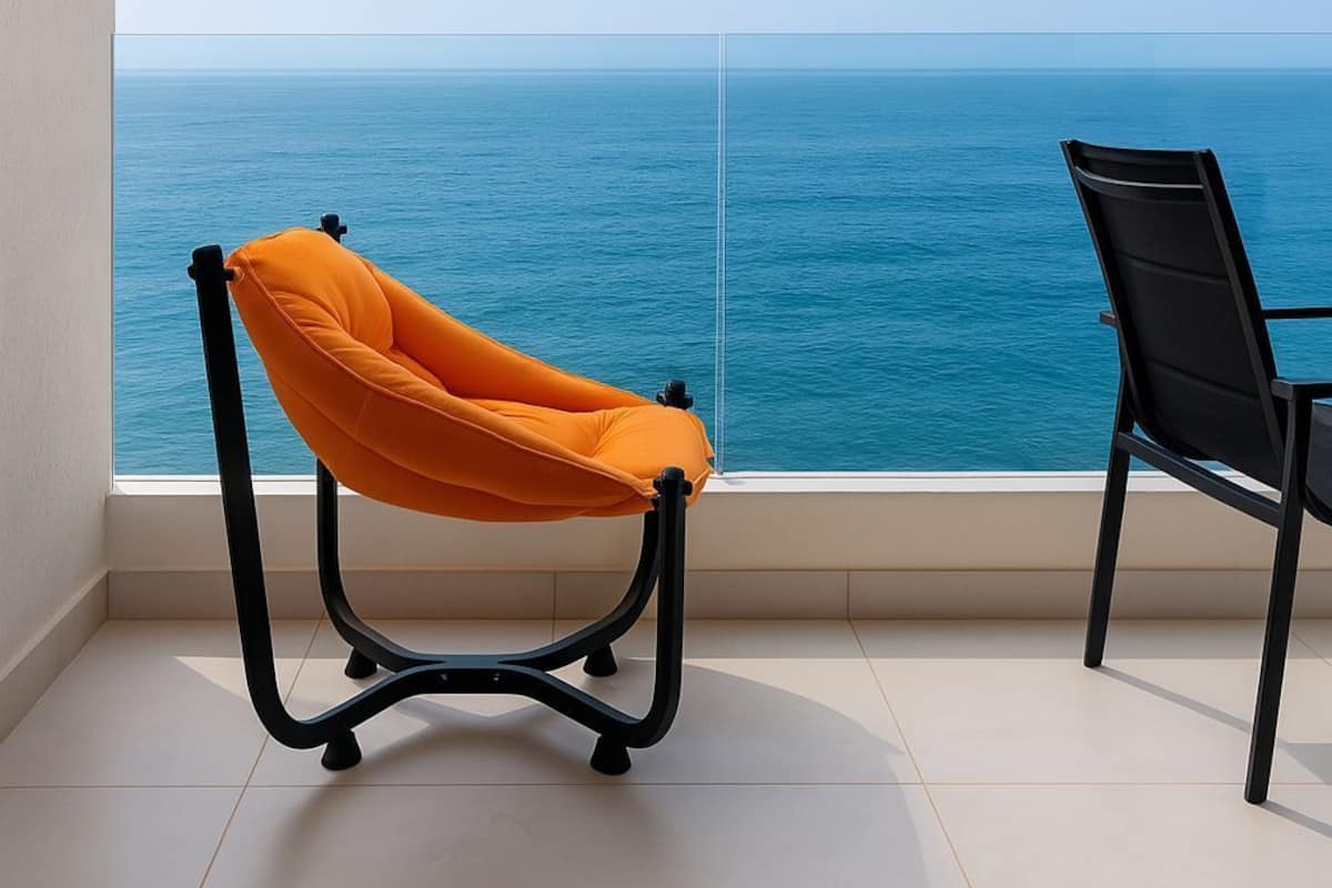 A balcony with a view of the sea, a black chair, and an orange chair.