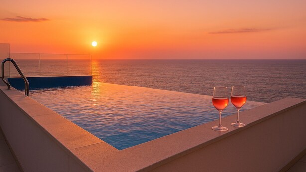 An infinity pool with a glass barrier, two glasses of red wine, and a sunset view over the ocean. - SeaRock Suites (Aamchit)