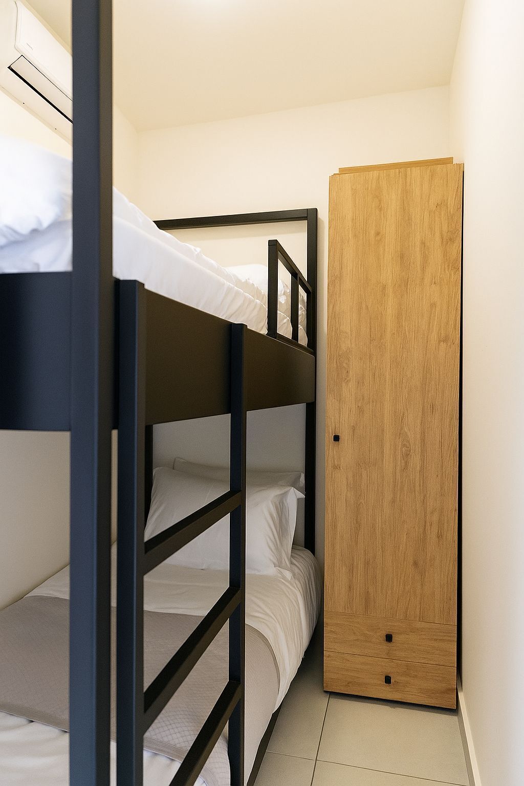 Une chambre avec des lits superposés, une armoire en bois et un climatiseur fixé au mur.