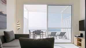 A modern living room with a sofa, a coffee table, and a TV. There is a balcony with a table and chairs, and a view of the sea. - SeaRock Suites (Aamchit)