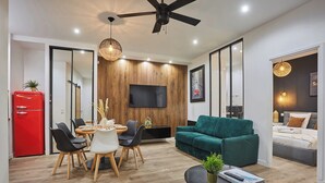 A modern living room with a wooden accent wall, a flat-screen TV, a teal sofa, and a dining area with a red refrigerator. - Sublime Flat in the Centre of Paris/montorgueil (Paris)