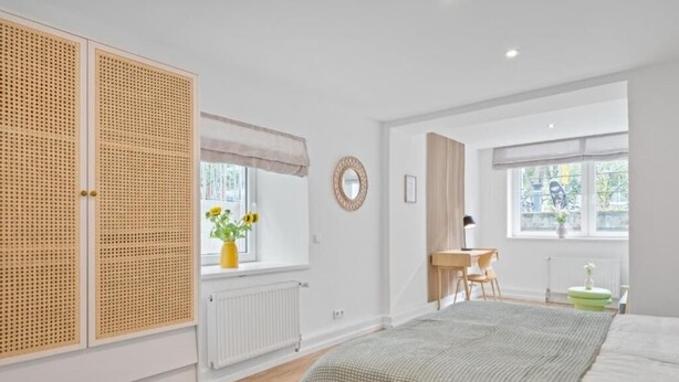 Een slaapkamer met een bed, een bureau, een stoel, een radiator en een raam met uitzicht.