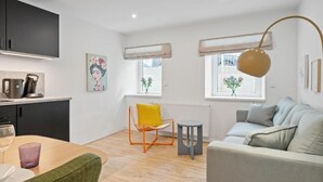 Een moderne woonkamer met een bank, een eettafel met stoelen, een keuken met kastjes en een raam met uitzicht.