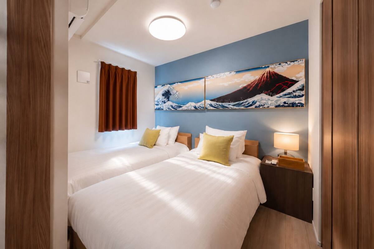 Une chambre d’hôtel avec deux lits, un tableau représentant une montagne, une table de chevet et une lampe.
