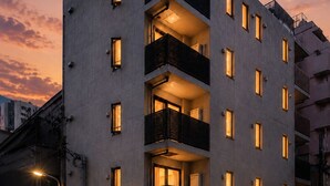 Un edificio de varios pisos con balcones, entrada principal y vista a la calle al anochecer.