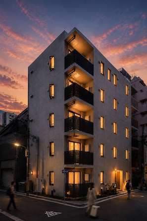 A multi-story building with balconies, a ground entrance, and a street view at dusk.