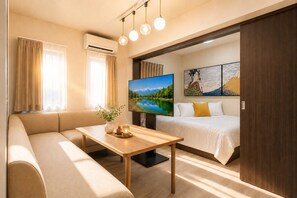 Una habitación de hotel moderna con sofá, mesa de madera, televisión de pantalla plana, cama y obras de arte en la pared.