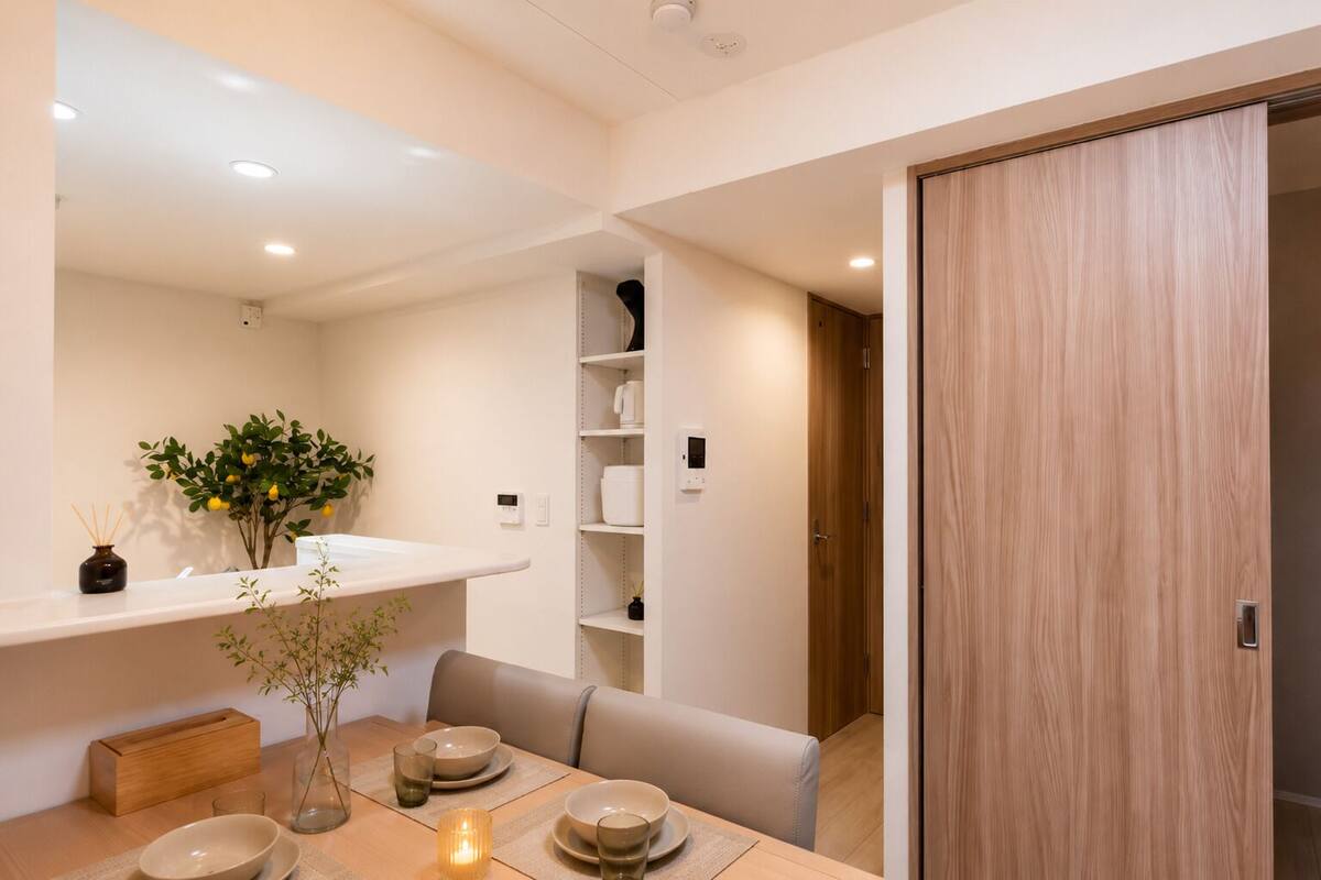 Un espace repas moderne avec une table en bois, des chaises, un vase avec des plantes et une étagère contenant des ustensiles de cuisine.