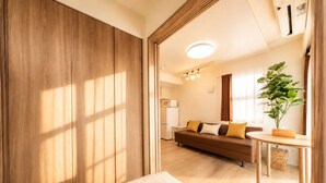 Una habitación moderna con un armario de madera, un sofá con cojines, una mesita con una planta y una cocina al fondo.