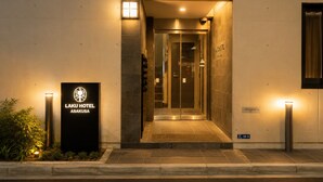 La entrada del hotel Laku Asakusa, con mostrador de recepción, puerta de cristal y un cartel.