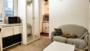 Un espace de vie compact comprenant un coin cuisine, un canapé avec des coussins et une table basse blanche.