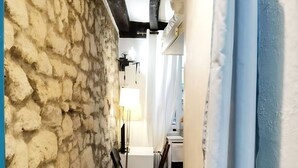 Un couloir étroit avec un mur en pierre, un bureau avec une lampe et une chaise.