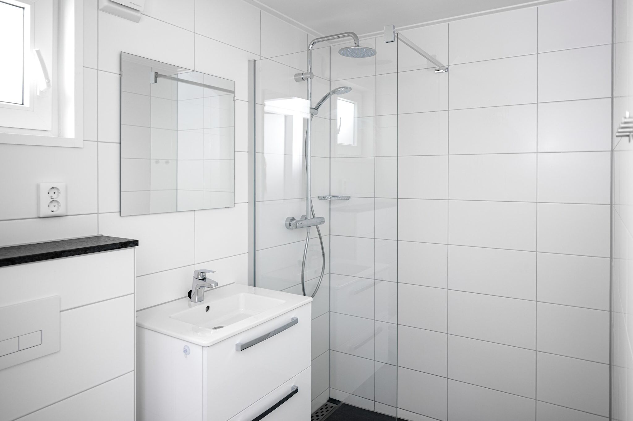 Une salle de bain moderne avec une douche à parois de verre, un lavabo blanc et un miroir au-dessus du lavabo.