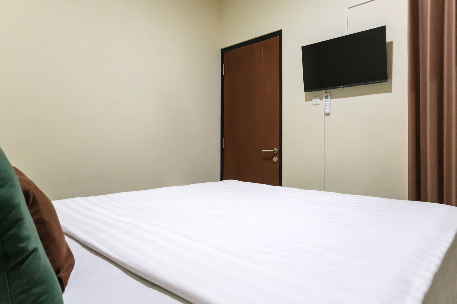 Een enkel bed in een kamer met een deur en een wandtelevisie.