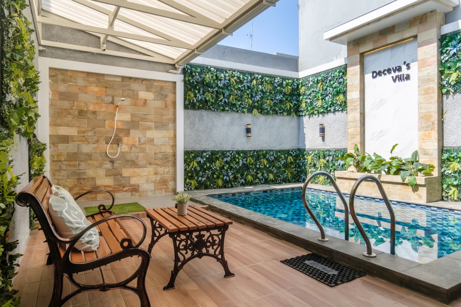 Zona de piscina amb una banca i una paret plena de vegetació.