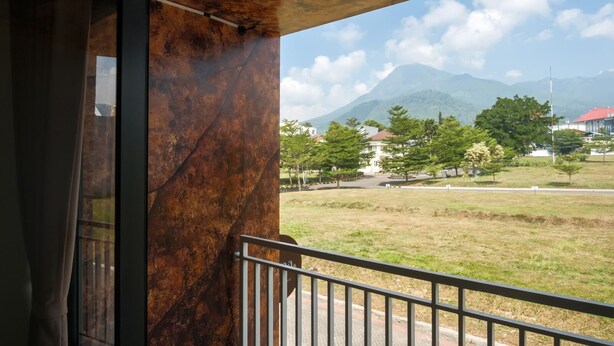 A balcony with a view of a grassy area, trees, and distant mountains. - Calma Villa Panorama, Batu Malang (Batu)