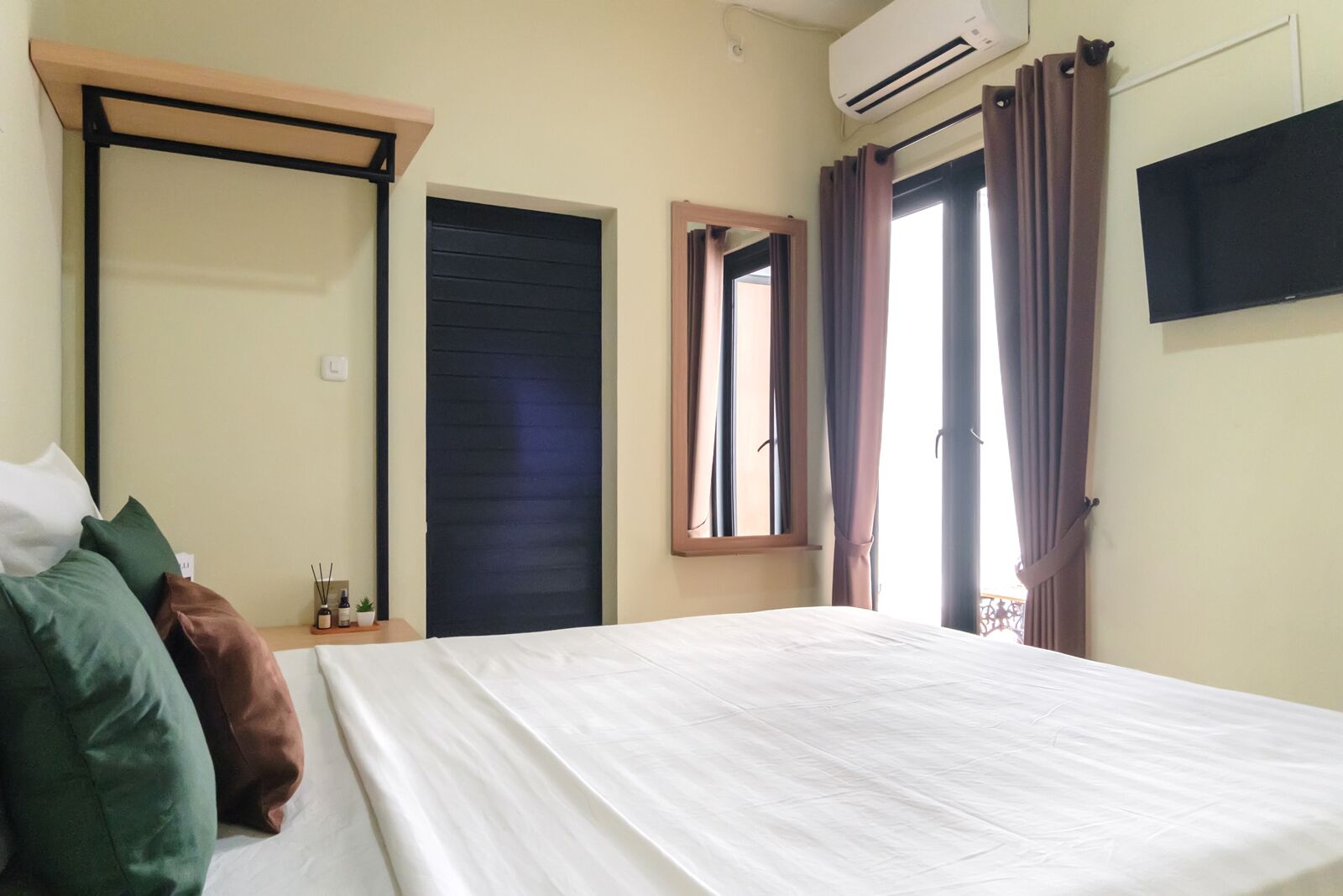 Habitación de hotel con cama, ventana con cortinas, unidad de aire acondicionado y televisión en la pared.